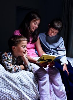 Getting caught up in the wonderful story. A sister reading to her younger brothers by lamplight in the bedroom.