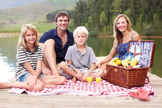 Picnicking lakeside with a smile. Happy young family having a picnic on a jetty by the lake.