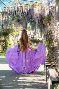 Thoughtful happy mature woman surrounded by chinese wisteria in purple dress