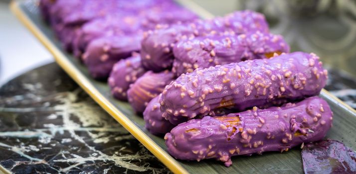Eclairs with sweet purple topping with nuts on serving plate