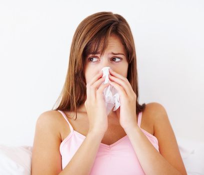 Young female with a cold blowing her nose. Cold and flu - Young female in bed blowing her nose.