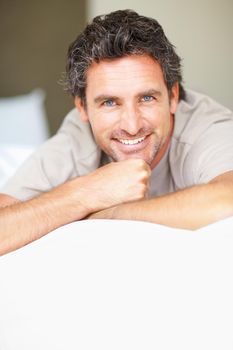 Handsome man resting on bed. Portrait of handsome man resting on bed and giving you an attractive smile.