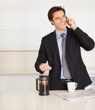 Young business man using cellphone while preparing coffee. Happy business man talking over cellphone while preparing coffee at home.