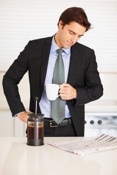 Young man reading newspaper while drinking coffee at home. Business executive reading newspaper while drinking a cup of coffee at home.