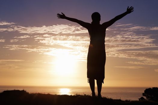 Enjoying life. Silhouette of a woman standing by sunrise with arms outstretched.