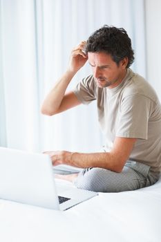 Thoughtful man using laptop. Thoughtful mature man looking at laptop while sitting on bed.