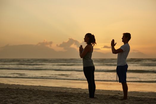 Enjoying the peace and tranquility of nature. a couple doing yoga on the beach at sunset.