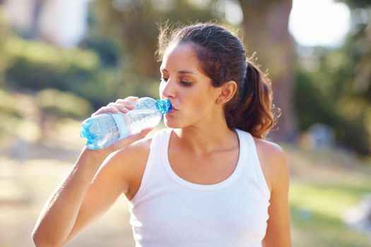 Woman drinking a bottle of water after jogging. Portrait of an attractive woman having a bottle of water after a jog.