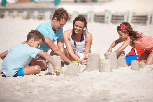 Planning the most magnificent castle ever...a happy family building sandcastles together at the beach.
