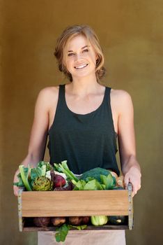 Grow the good life. A young woman holding a crate of vegetables outdoors.