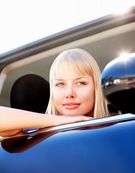 Smiling thoughtful female with head out of a car. Thoughtful - Cute blond female relaxing on a cars window.