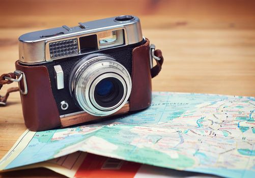 Time to go see the sights and capture them. Closeup shot of an old-fashioned camera and a map lying on a wooden table.