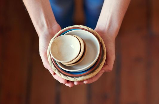 Beautiful ceramic kitchenware. a young woman holding a stack of ceramic bowls in her kitchen.