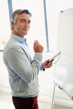Were exceeding our targets this month. Portrait of a mature business standing at a whiteboard holding a notebook.