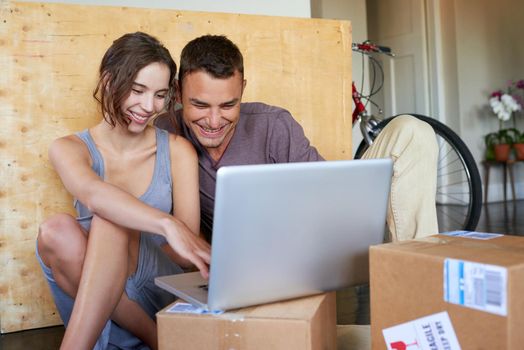 Keeping their social network posted with moving day updates. an affectionate young couple using a laptop on the floor at home.
