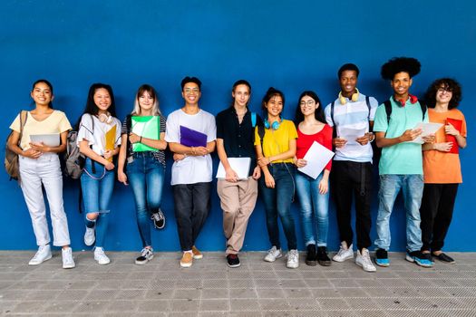 Group of multiracial teenage high school students looking at camera standing on blue background. Back to school.