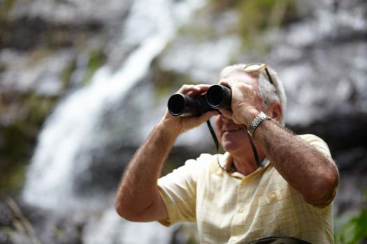 Exploring the landscape. a senior man looking at scenery with a pair of binoculars.