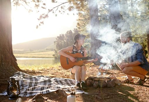 Campfire tunes. a young woman playing guitar for her boyfriend at their campsit.
