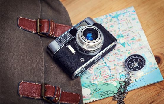 Make life a daring adventure. a camera, map, compass and bag on a wooden table.