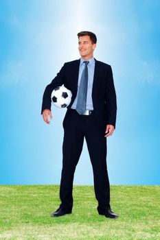 Young executive with a football in hand looking at copyspace. Happy young business man on field holding a soccer ball and looking at something interesting.