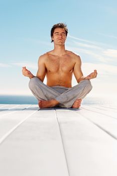 Shirtless man meditating while isolated on a porch. Portrait of a handsome young man practicing yoga in the lotus position on a porch.