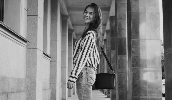 Street Style Outdoors Portrait of Beautiful Girl. Fashion Woman Smiling. She wearing Print Shirt, Jeans, Bag. Lifestyle