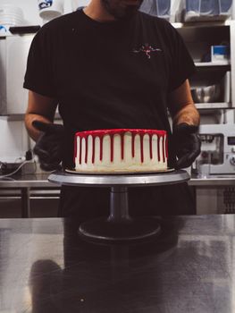 cake designer decorating a red drip cake with berries on the top