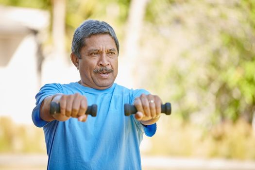 Staying strong and active. a mature man lifting dumbbells outside.