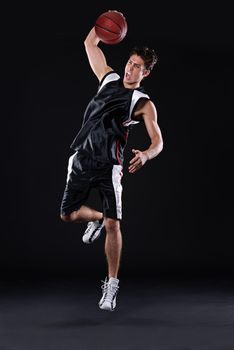 Shooting some hoops. Full length shot of a male basketball player in action against a black background.