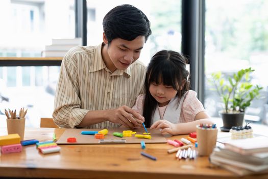 Young asian father and daughter plasticine or play dough on a table dough together