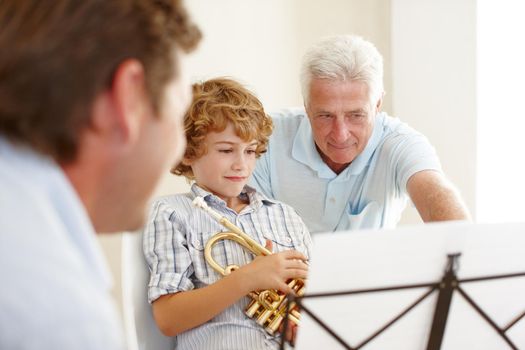 Passing on his musical wisdom. a grandfather teaching his grandson how to play the trumpet while his father looks on.