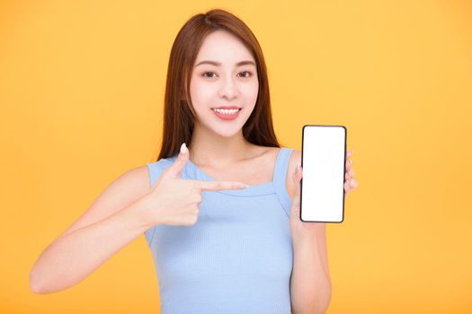 Happy asian woman showing mobile phone blank screen on yellow background