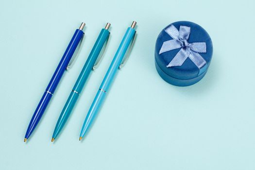 Three plastic pens and gigt box on a blue background.