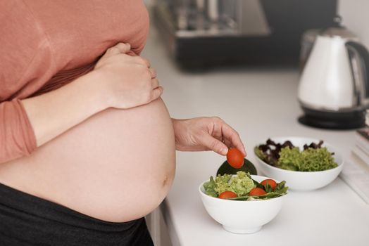 Making the healthy choice for baby and me. a young pregnant woman eating a salad in the kitchen.