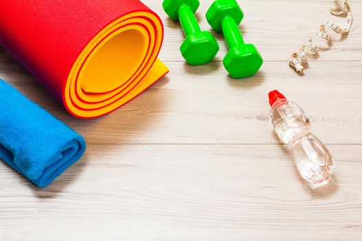 Yoga mat, a towel, a bottle of water, a measuring tape and dumbbells in a room or a gym on the gray floor.