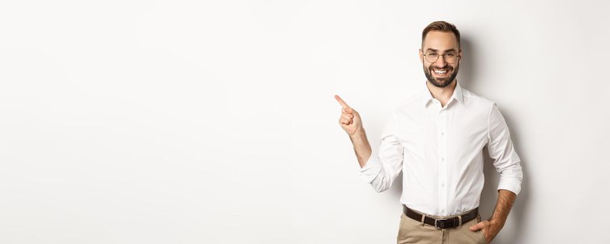 Confident businessman pointing finger left at company logo, standing over white background