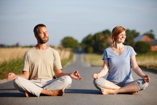 Finding inner peace together. a serene couple sitting in the lotus position on a country road.