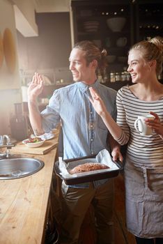 Nothing says home like the smell of baking. a young couple waving through their kitchen window.