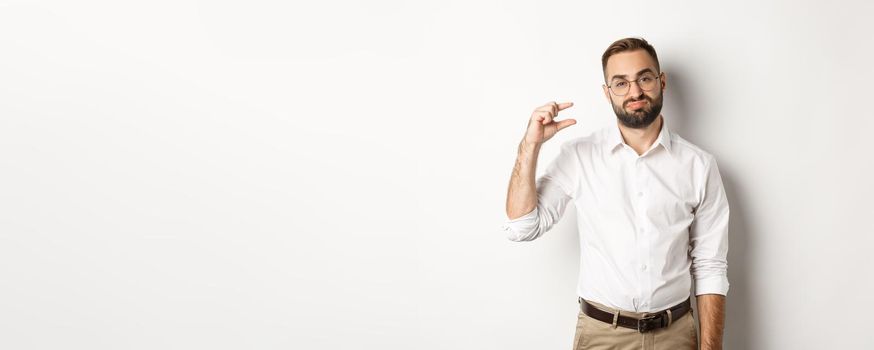 Disappointed male entrepreneur showing small object and sighing, standing over white background