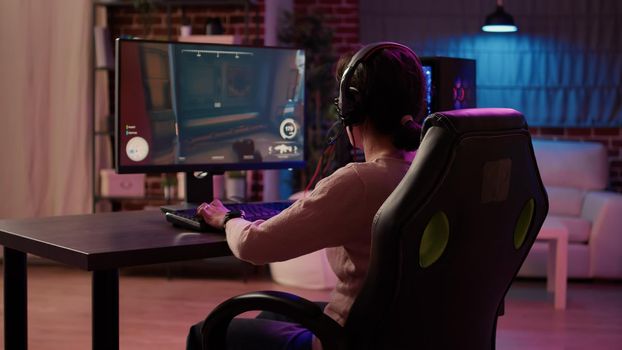 Gamer girl using pc gaming setup relaxing playing multiplayer online action game talking using headset