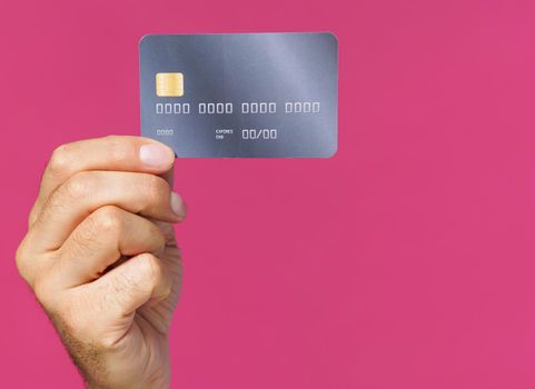 Great offer. Dark grey-purple debit, credit card in man hand isolated on pink background. Financial, banking concept. No face visible