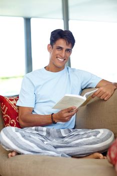 Sleep less, read more. a handsome young man sitting on his sofa while reading a book.