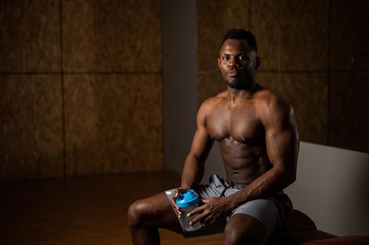 Shirtless african american man drinking from a shaker in the gym.