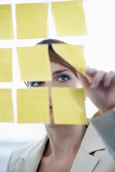 Visualizing her thoughts. a businesswoman arranging sticky notes on a glass wal.