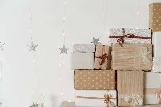Pile of Christmas gifts in colorful wrapping with ribbons against a white wall with silver stars.