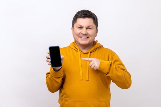 Middle aged man pointing finger at smartphone with empty screen, looking at camera with smile.