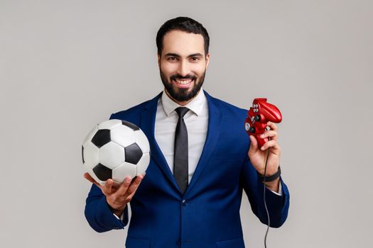 Delighted bearded man holding joypad and soccer black and white classic ball, football video game.