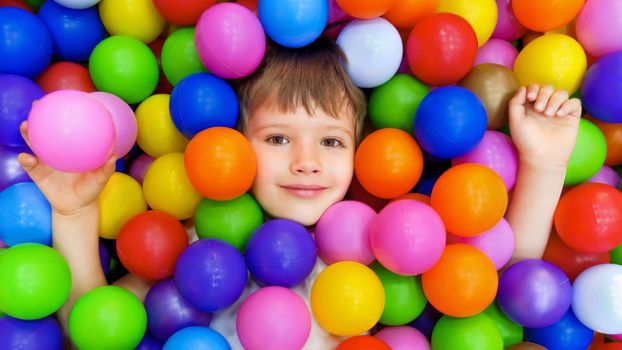 Smile kid lying colorful plastic balls pool. Colorful balls dry pool kindergarten playground child indoor play area. Playroom kids ball pit. Caucasian boy indoor playground kids play zone or kids zone