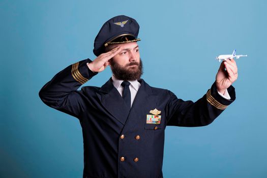 Pilot in uniform saluting to small airplane model