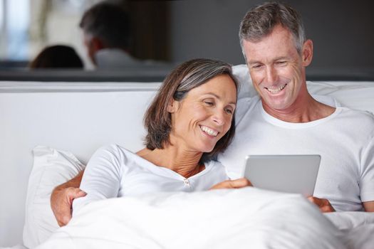 Entertainment in bed. a happy mature couple sitting in bed with a digital tablet.
